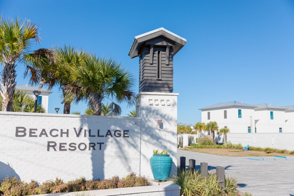 picture of the entrance to beach village resort with the name on stone near palm trees