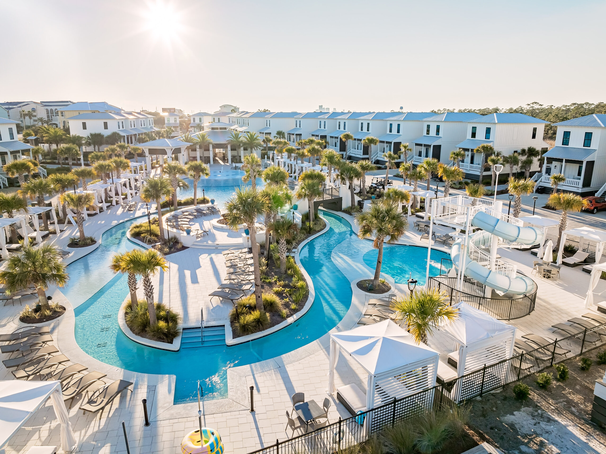 birds eye view picture of the beach village resort with the sun over the property of buildings and a lazy river