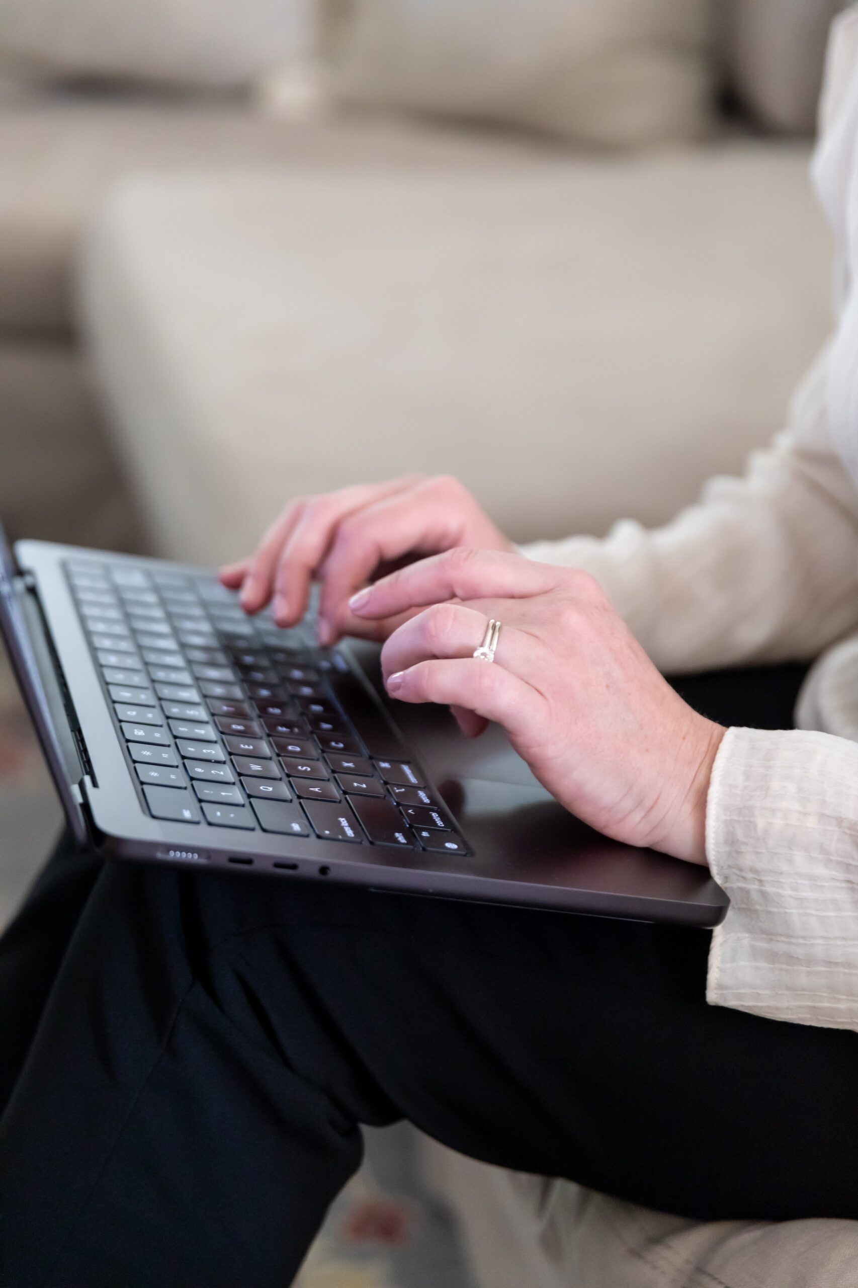 woman's hands typing on a computer sitting on a sofa